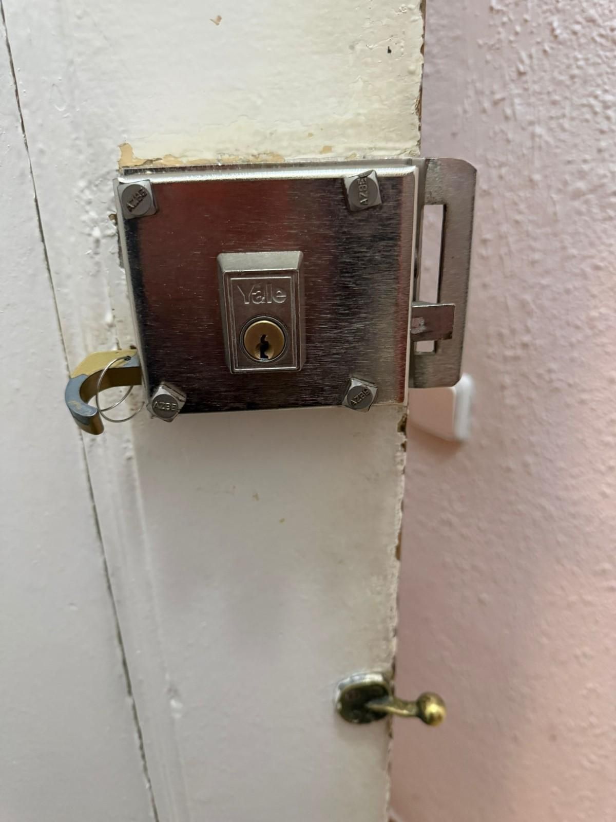 Primer plano de un pestillo y una cerradura metálicos montados en una puerta pintada de blanco.