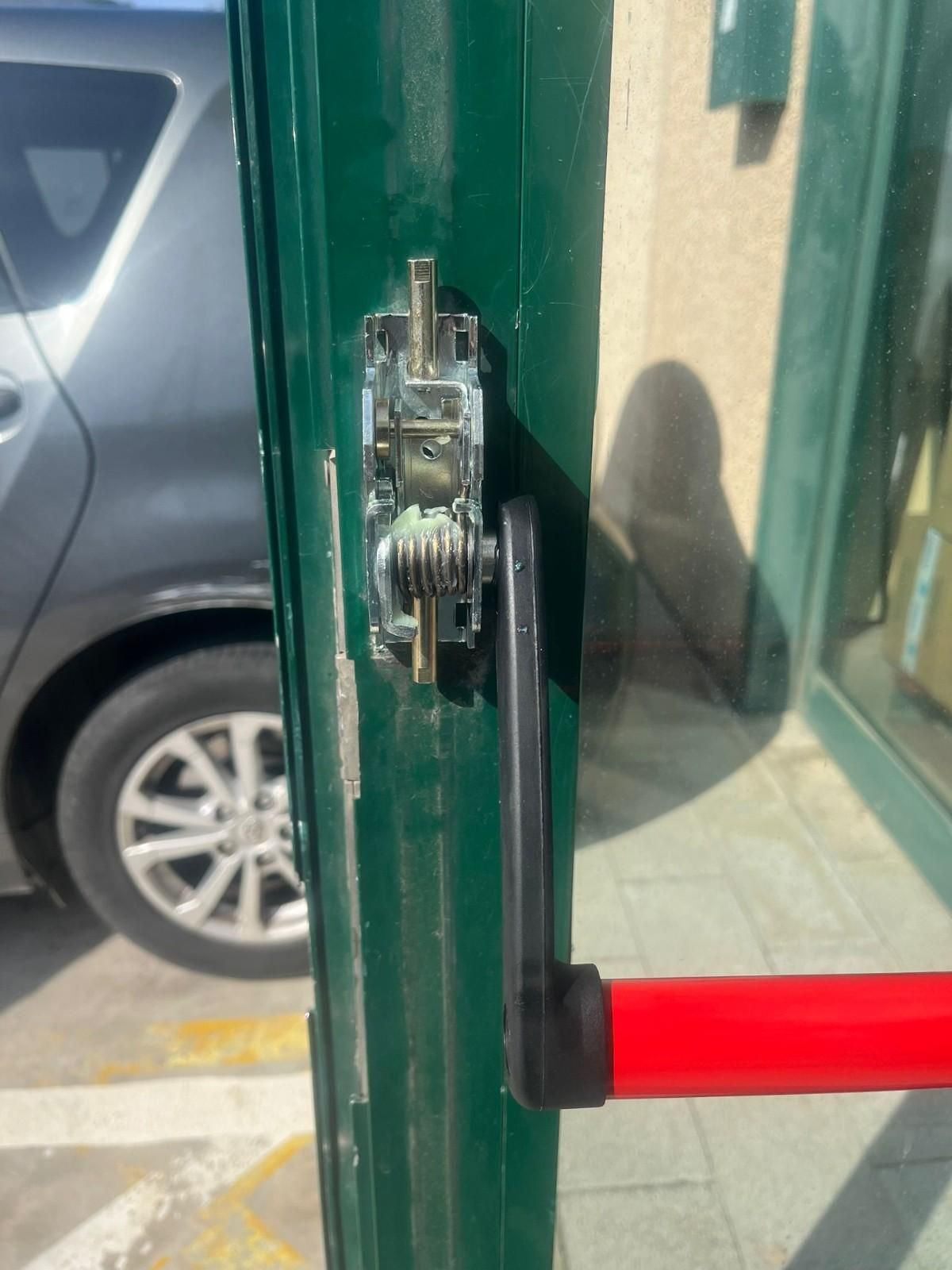 Primer plano de un pestillo y una manija de puerta verdes rotos junto a una puerta de cristal.