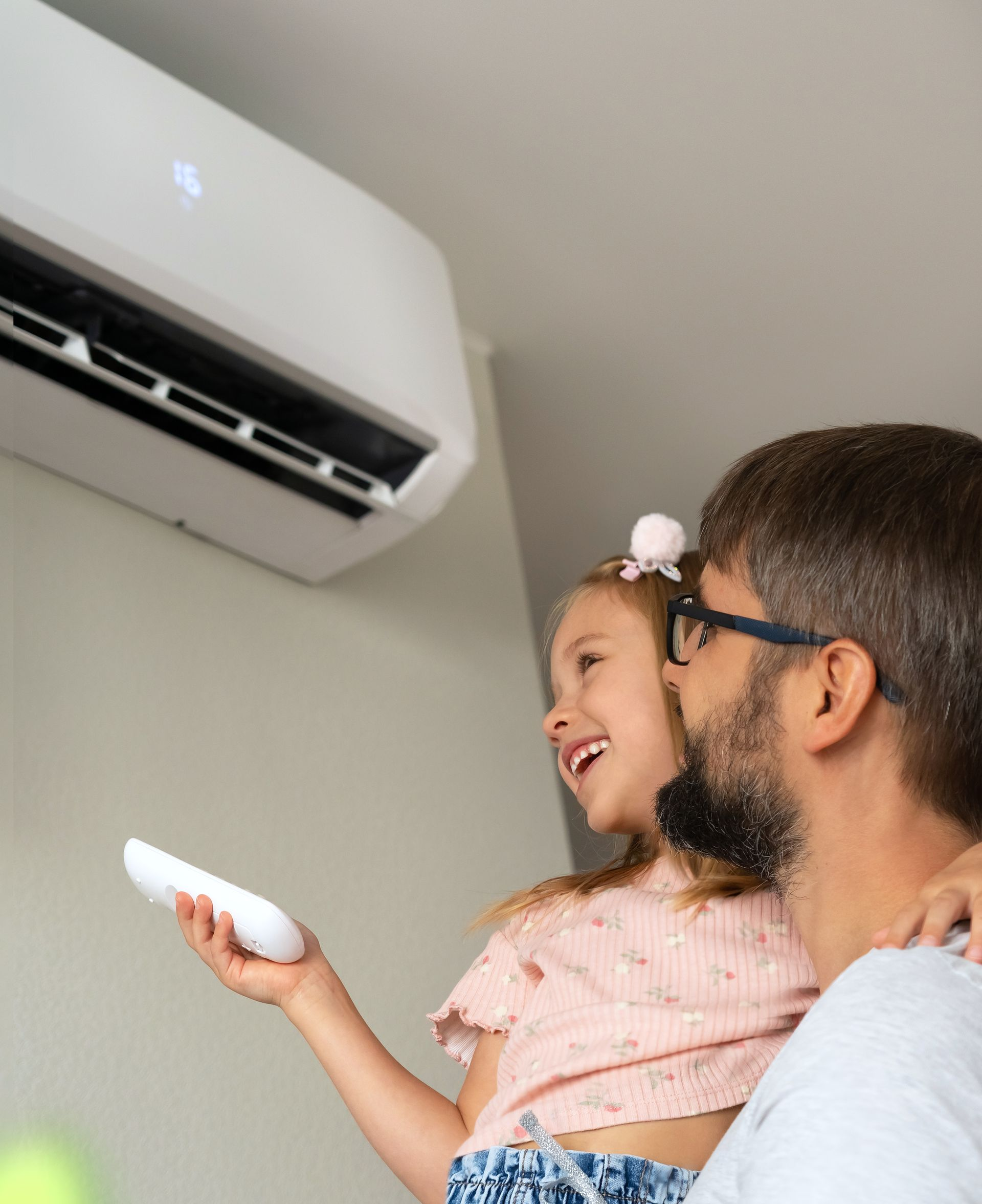 Un homme avec sa fille tenant la télécommande en direction de la climatisation