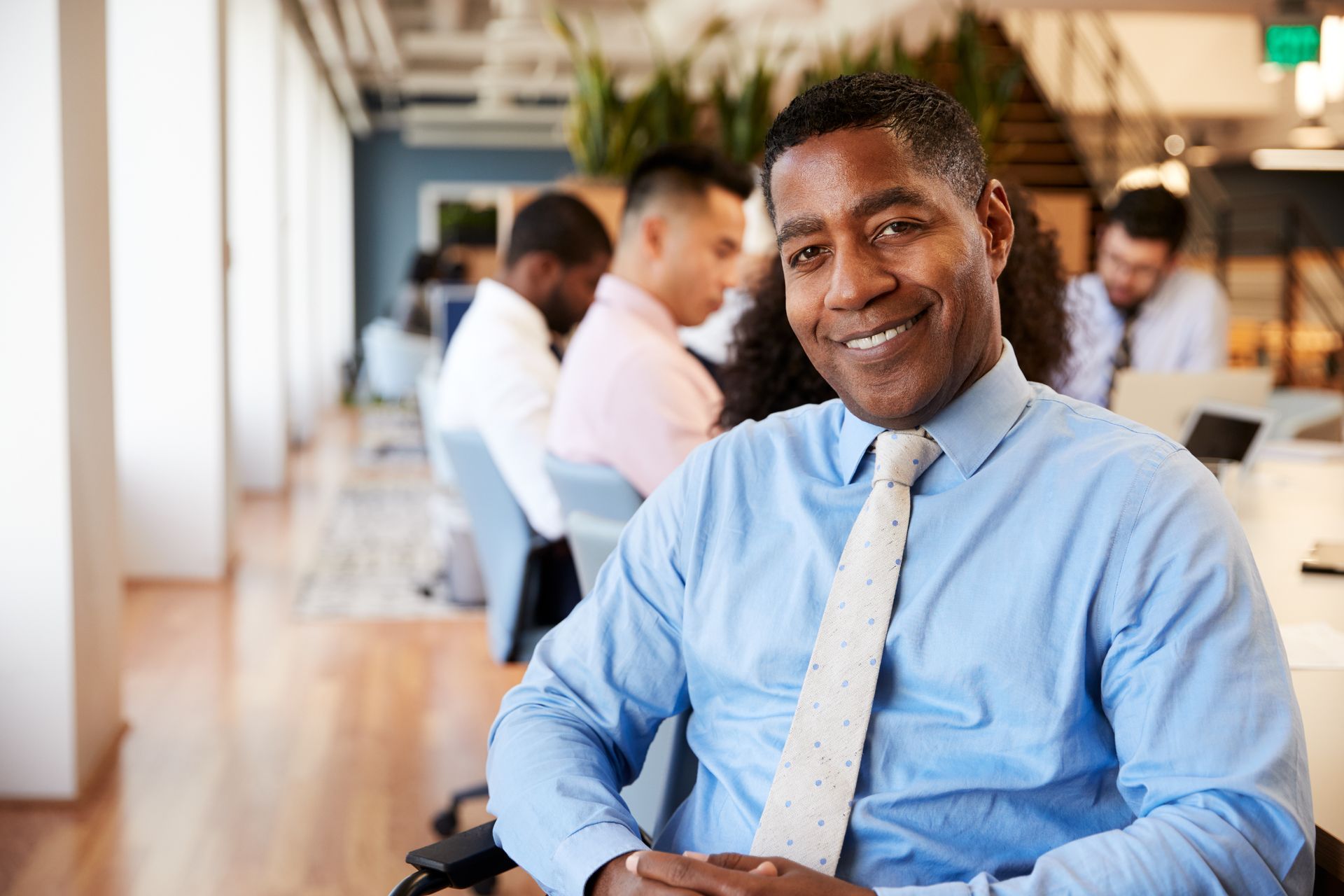 Ein Mann in blauem Hemd und Krawatte sitzt in einem Büro.