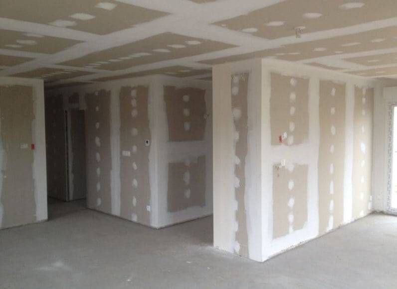 Intérieur inachevé avec des cloisons sèches aux joints enduits, une structure de plafond apparente et un sol en béton