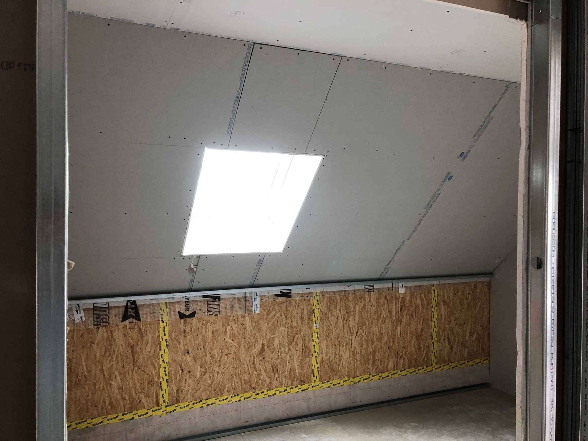 Plafond en pente avec un puits de lumière lumineux et des panneaux muraux en contreplaqué brut dans une pièce