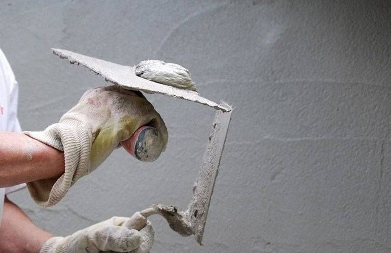 Main gantée appliquant du plâtre gris dans un angle de mur à l’aide d’une truelle