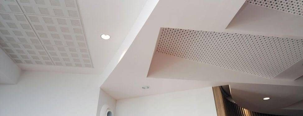 Plafond blanc avec des spots encastrés et des panneaux perforés dans un couloir moderne