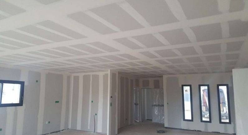 Intérieur en plaques de plâtre vide en construction, avec plafond jointoyé, murs blancs, plusieurs fenêtres et portes.