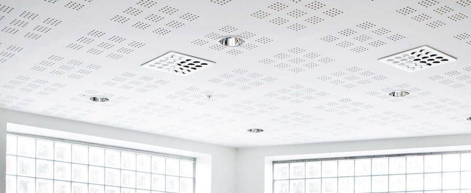 Pièce d’un blanc éclatant, avec de grandes fenêtres et un plafond à motifs doté de bouches d’aération et de luminaires