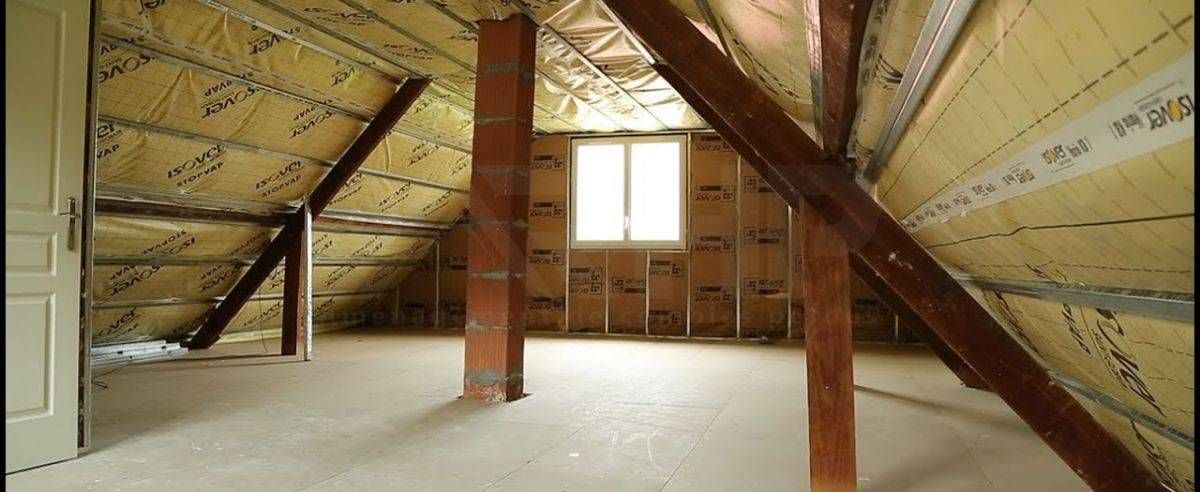 Combles non aménagés avec poutres apparentes, isolation et petite fenêtre au fond