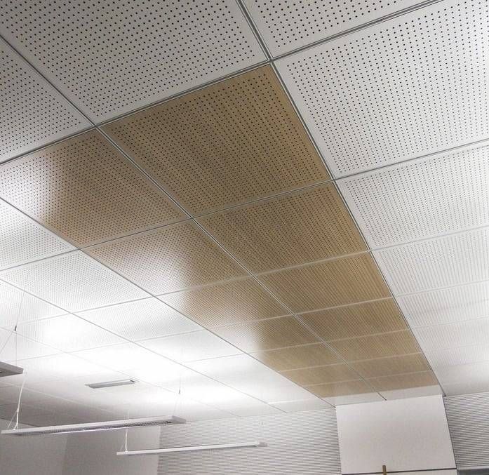 Plafond intérieur avec un grand panneau acoustique marron parmi des dalles de plafond blanches et des luminaires fluorescents