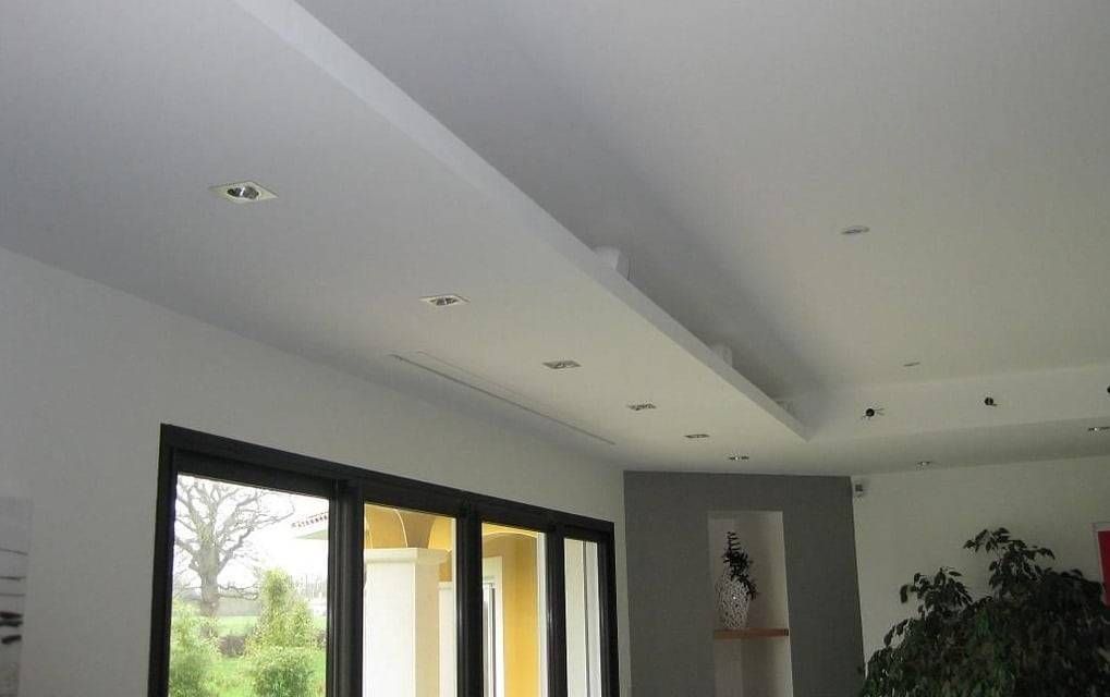 Salon moderne avec plafond blanc, spots encastrés, fenêtres à cadre noir et mur d’accent sombre orné d’œuvres d’art.