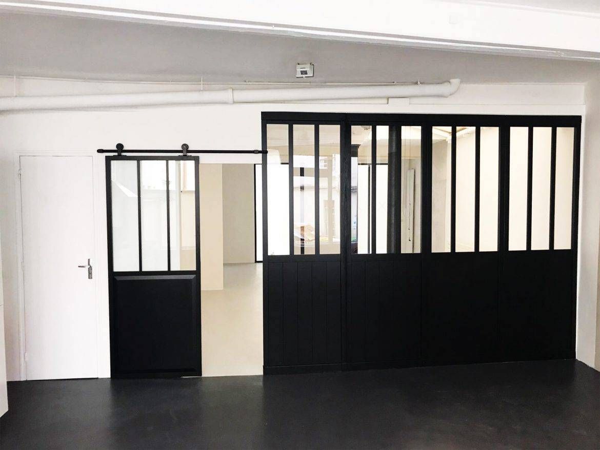 Pièce vide avec des murs blancs, un sol noir et des portes de séparation à cadre noir le long d’un côté