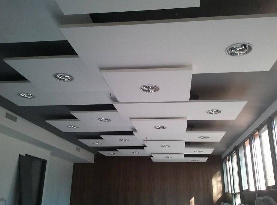 Plafond moderne avec des spots encastrés et des panneaux blancs superposés dans une pièce aux hautes fenêtres