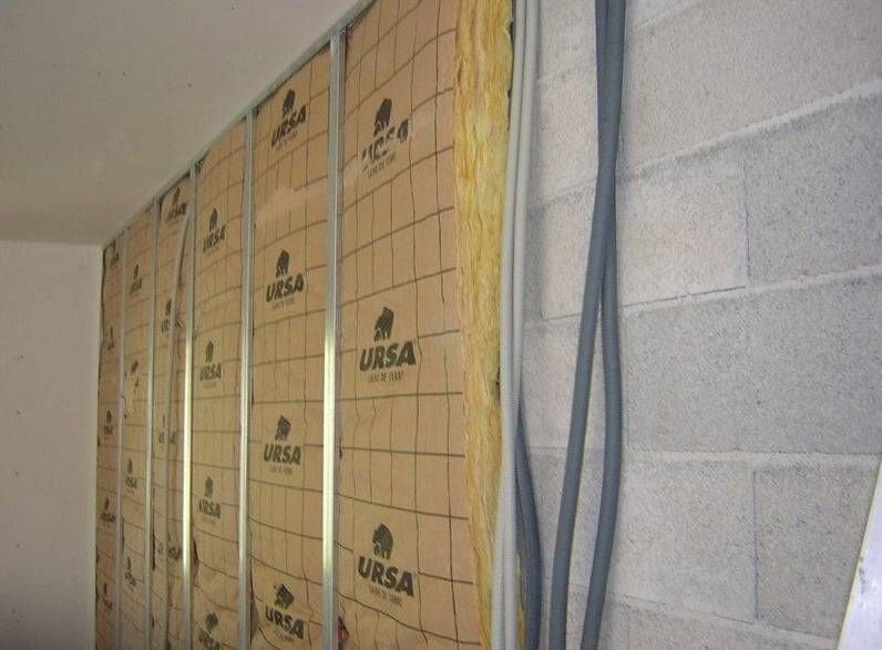 Mur isolé avec des panneaux URSA jaunes et des câbles bleus apparents dans un intérieur en construction