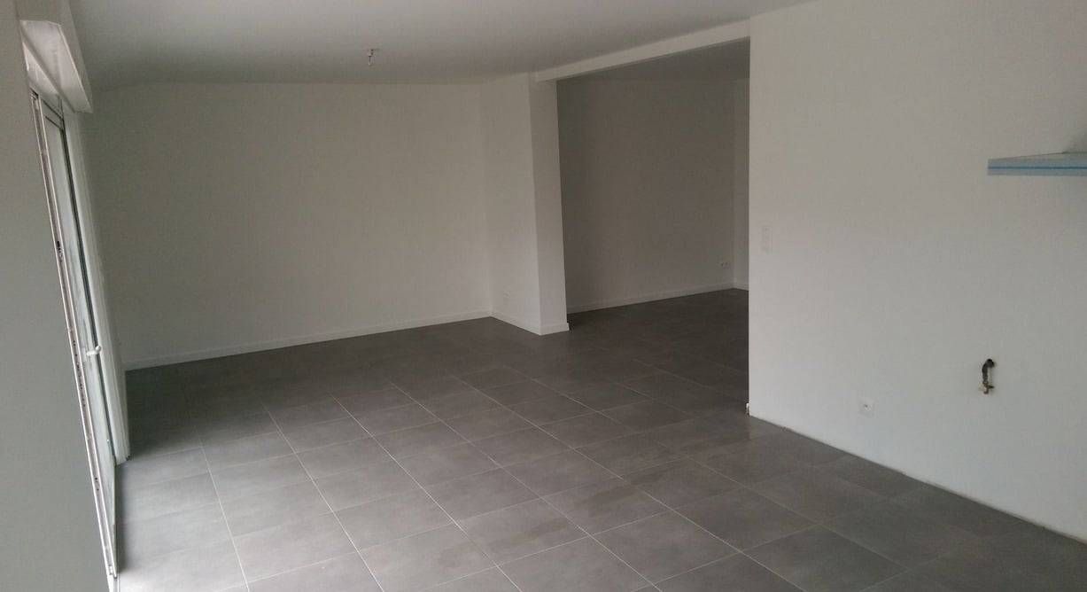 Pièce vide et non meublée, avec un sol carrelé gris, des murs blancs et une porte donnant sur une autre pièce