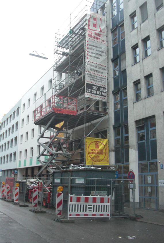 Ein eingerüstetes Bürogebäude während der Fassadendemontage mit einer mobilen Arbeitsplattform.