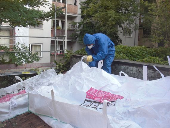 Ein Arbeiter in Schutzkleidung legt Plastikplanen zur Abschottung bei Schadstoffsanierung aus.