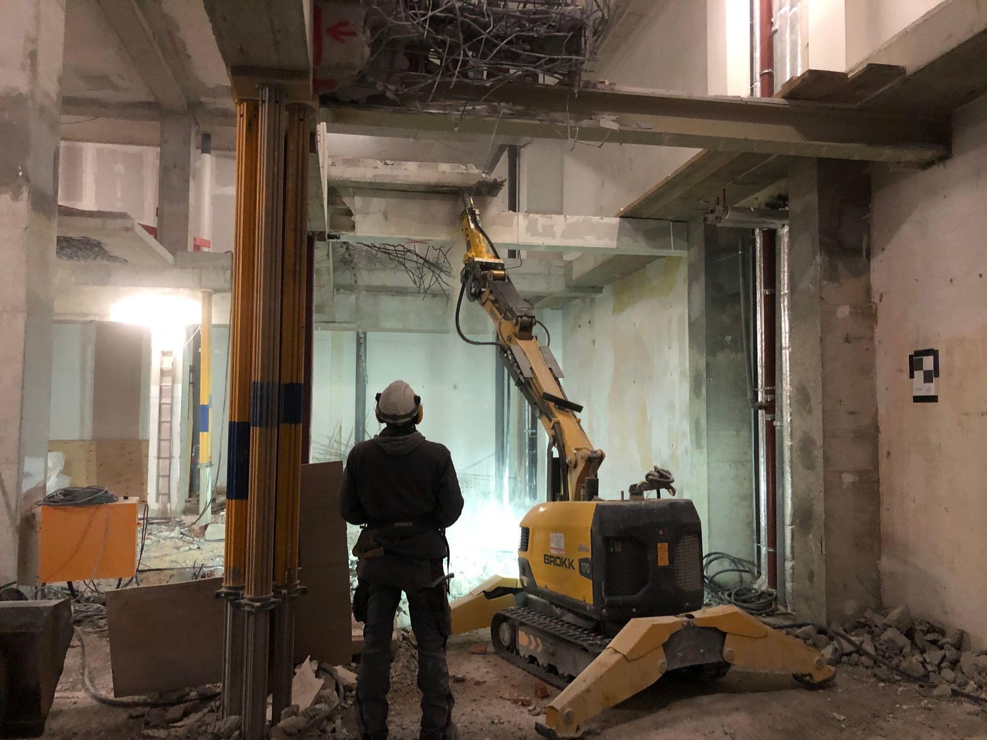 Ein Arbeiter bedient per Fernsteuerung einen Abbruchroboter im Innenraum eines Gebäudes.