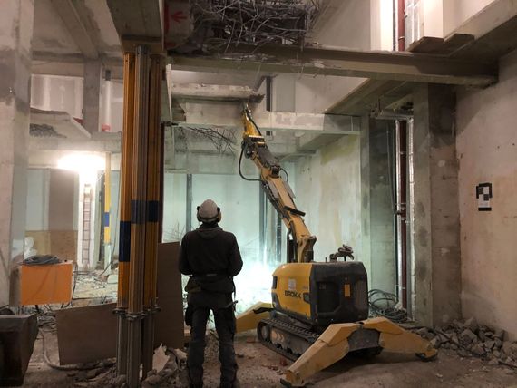 Ein Arbeiter steuert per Fernbedienung einen modernen Abbruchroboter im Innenraum.