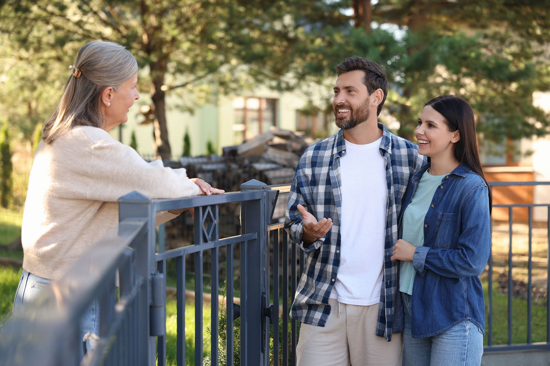 Une femme appuyée contre une clôture discute avec un couple dehors. Ils sourient.