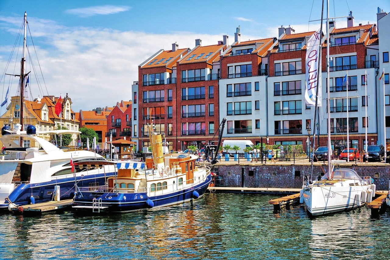 Grupa łodzi zacumowanych w porcie, w tle widoczne budynki.