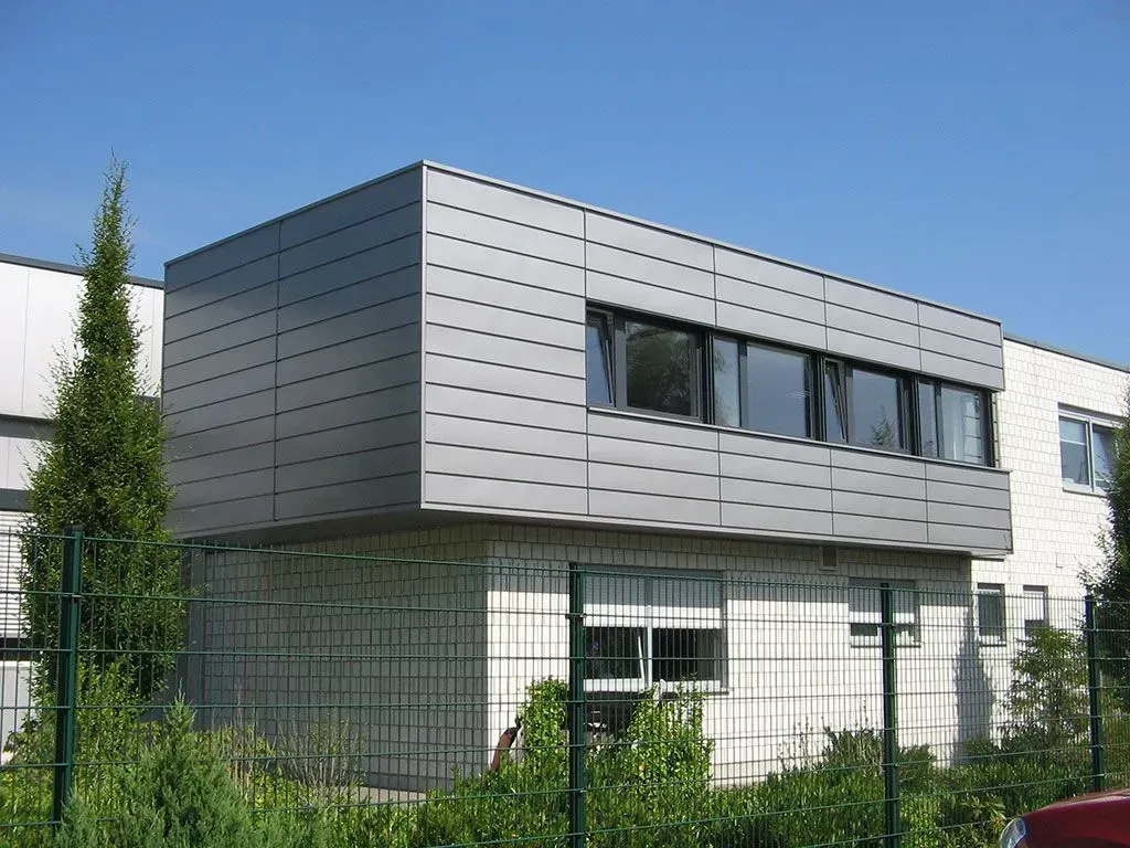 ein großes Gebäude mit vielen Fenstern und einem grünen Zaun davor