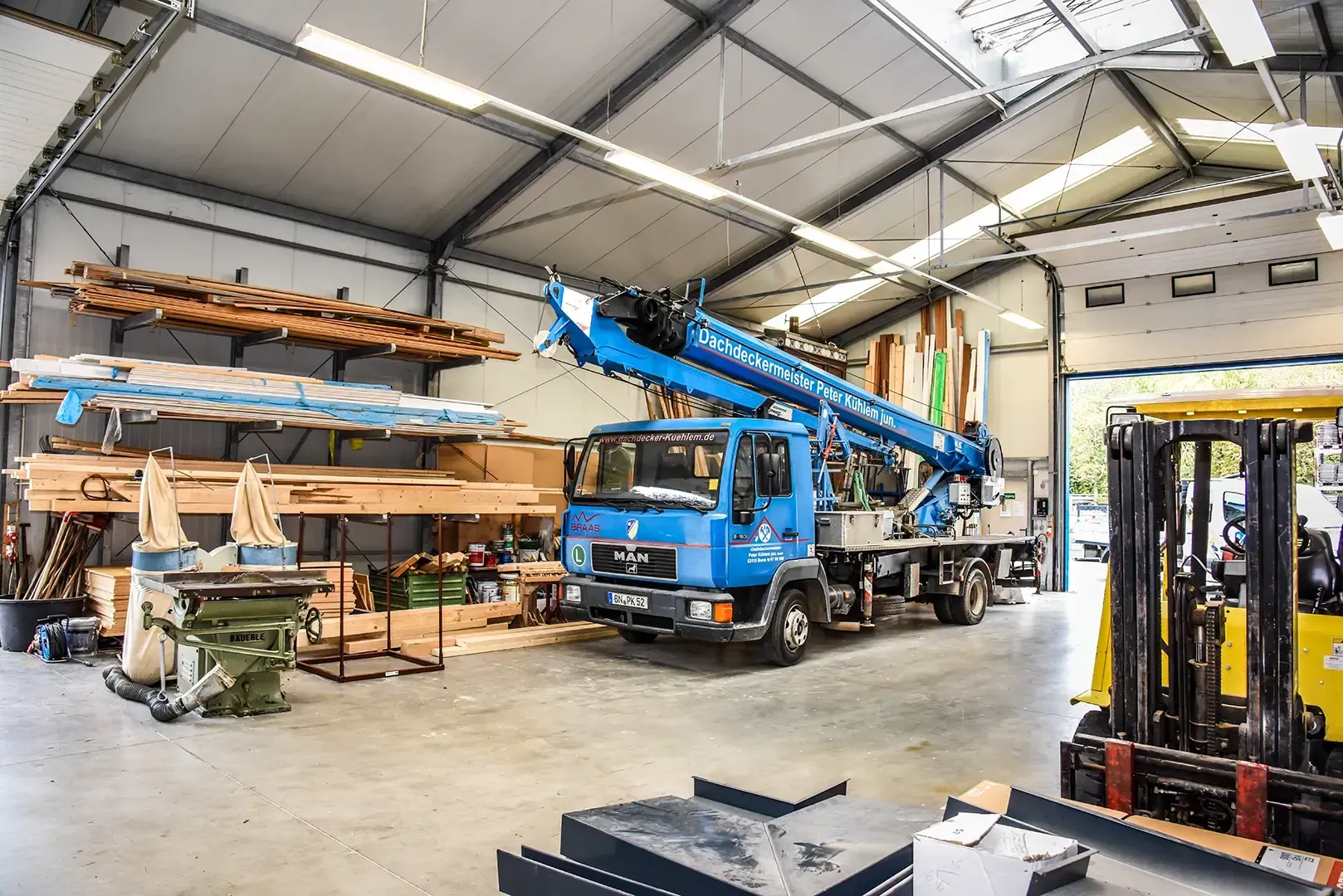 Ein blauer Kran erstreckt sich bis zu einem mehrstöckigen Gebäude an einer Straße, davor ist ein Auto geparkt.
