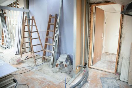 Mann im blauen Overall benutzt während der Renovierung eine Wasserwaage an der Außenseite eines weissen Hauses. Gerüst ist sichtbar.
