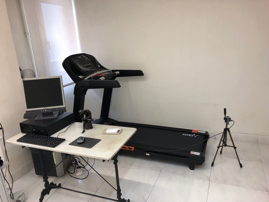 Una cinta de correr está colocada sobre un escritorio al lado de una computadora.