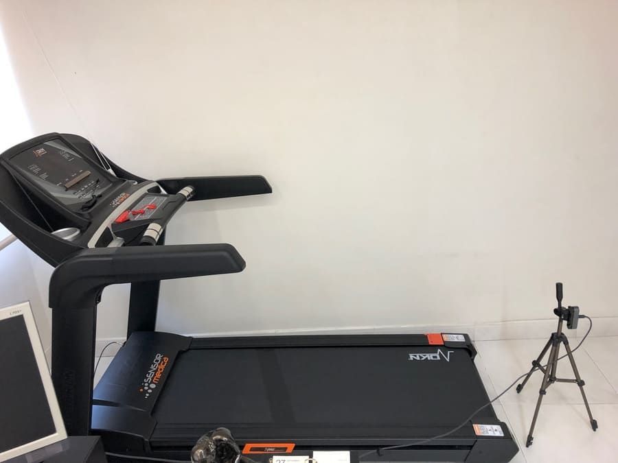 Una cinta de correr está colocada en una habitación al lado de una computadora y un trípode.