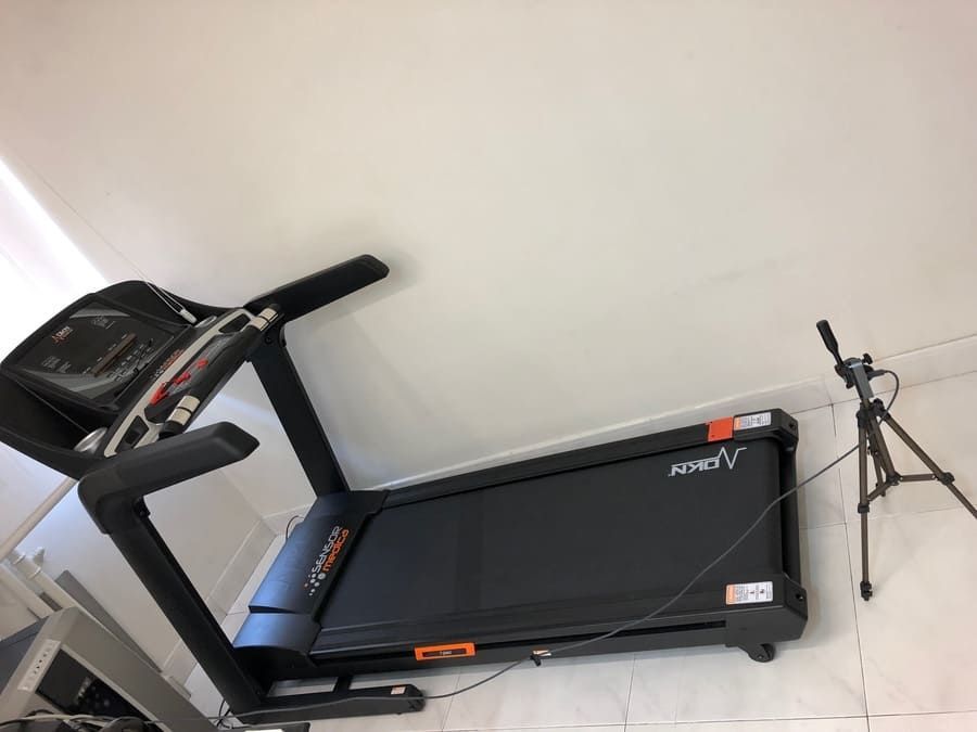 Una cinta de correr está colocada en el suelo al lado de un trípode.