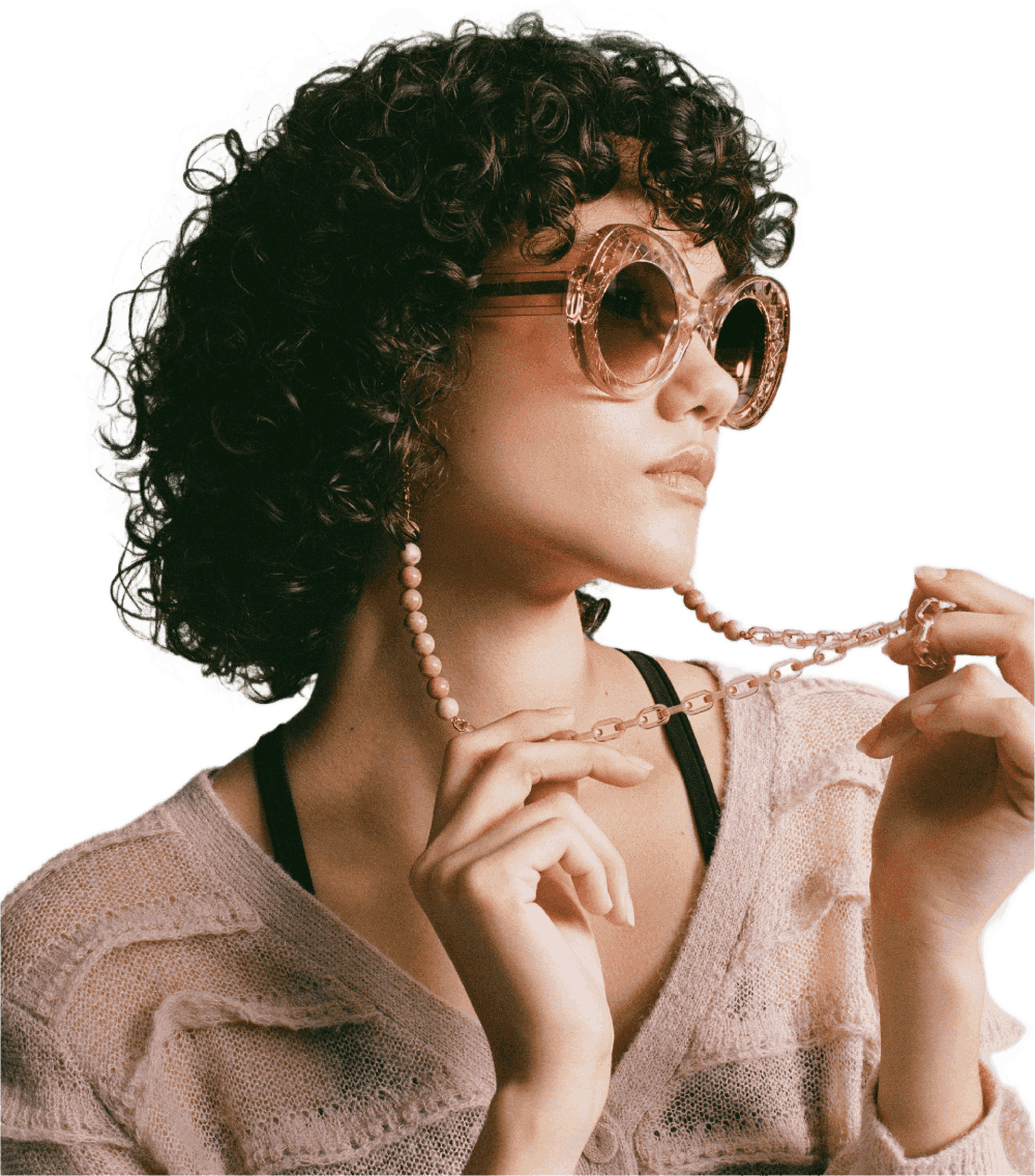 Eine Frau mit lockigem Haar, einer Sonnenbrille und einer Perlenkette