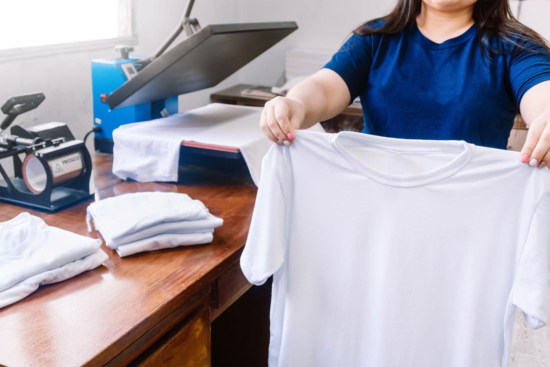 Mujer sosteniendo una camiseta blanca, preparándola para imprimirla