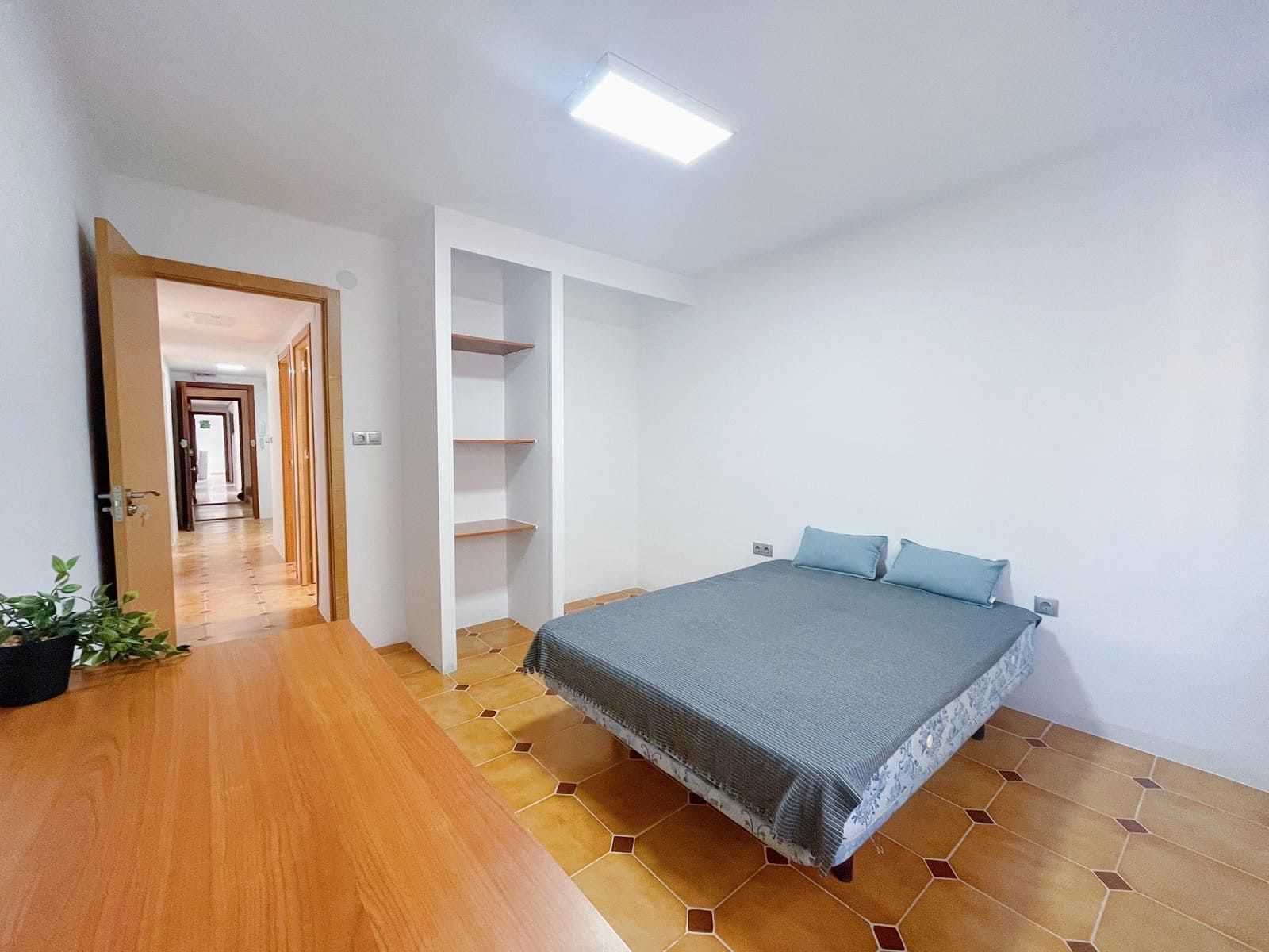 Dormitorio con cama, estantes empotrados, escritorio de madera y puerta abierta que conduce al pasillo.