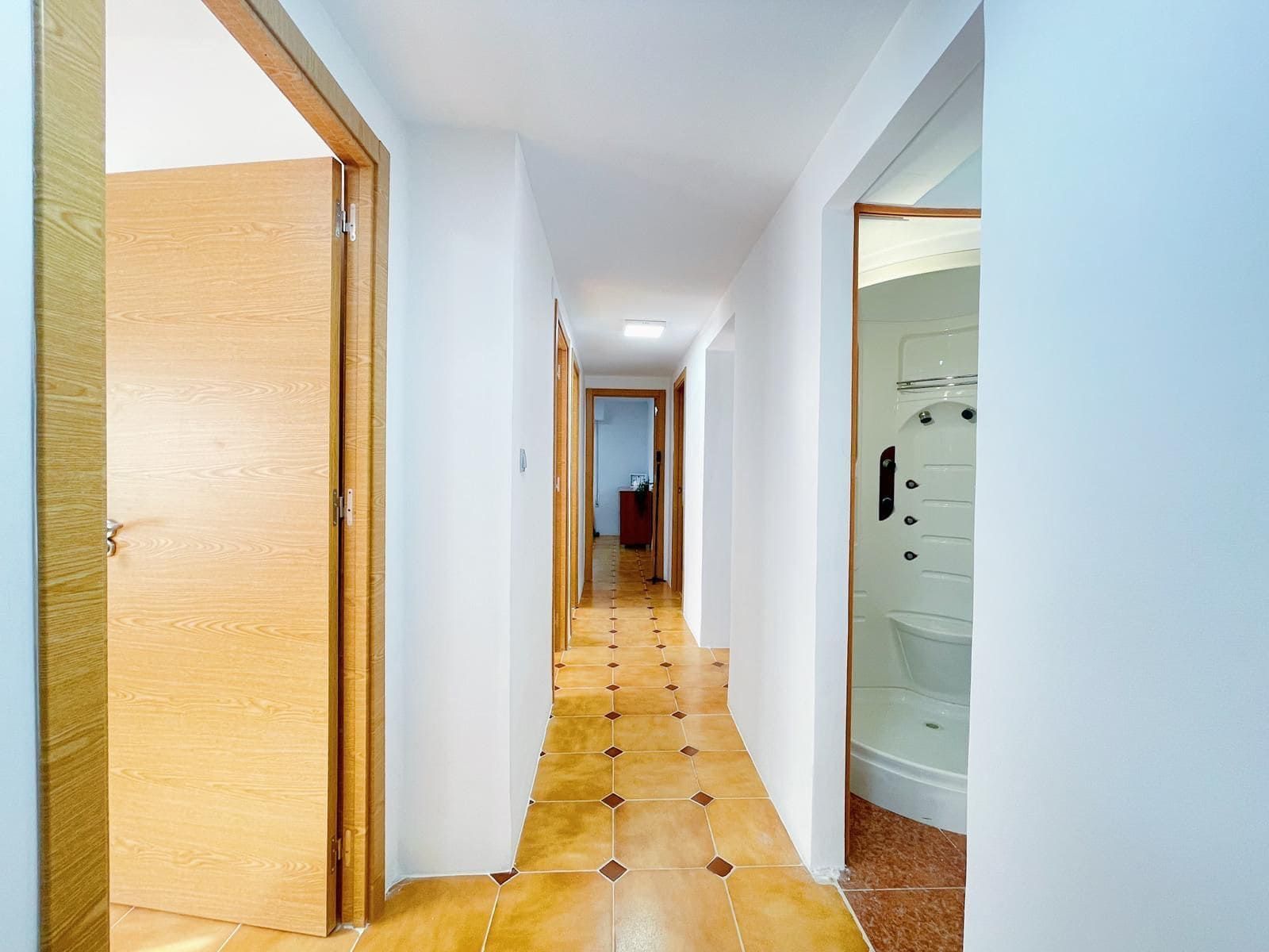 Pasillo estrecho con puertas de madera y suelo de baldosas.