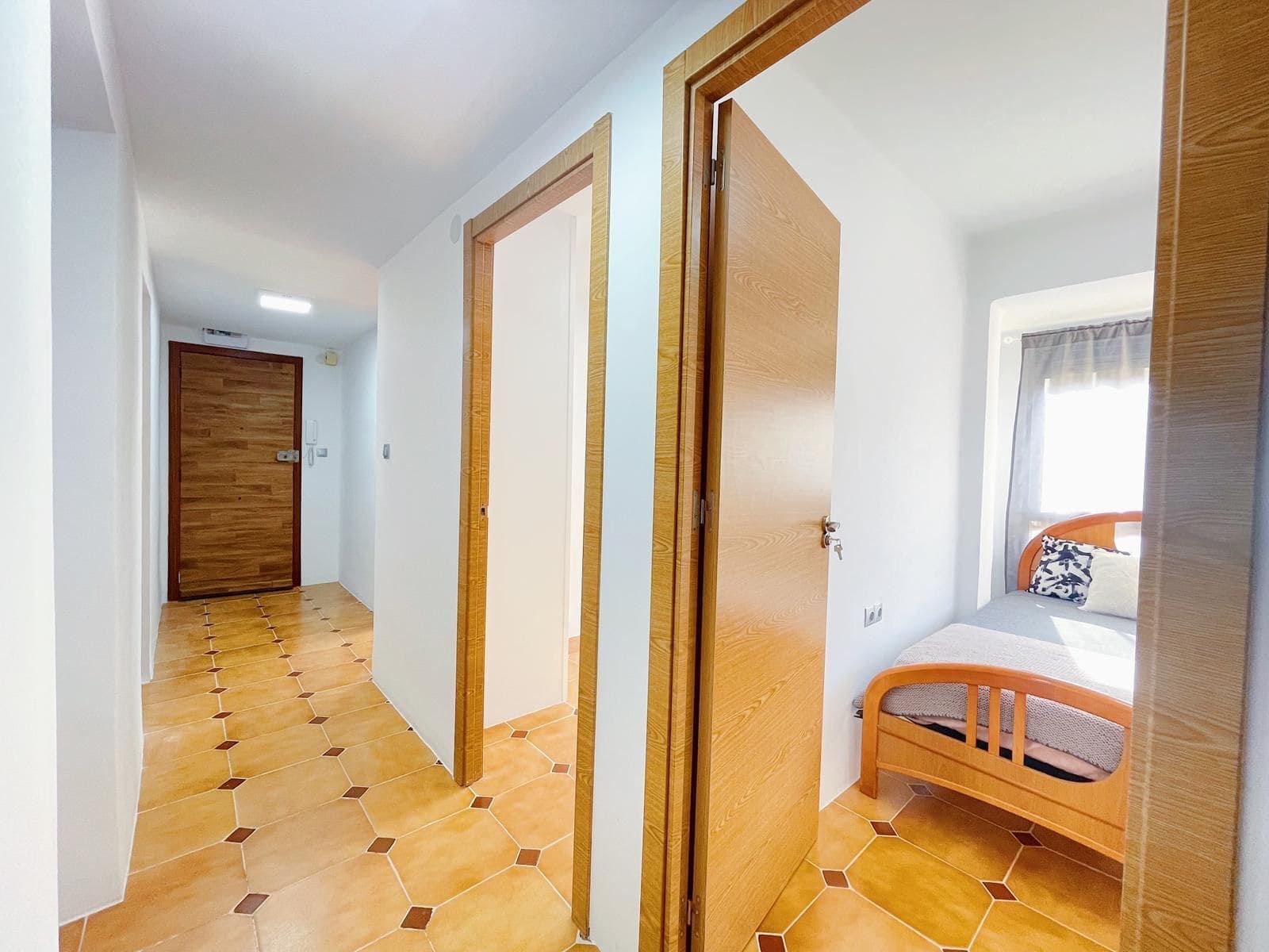 Pasillo con suelo de baldosas, puertas a las habitaciones a ambos lados, una abierta a un dormitorio con cama.