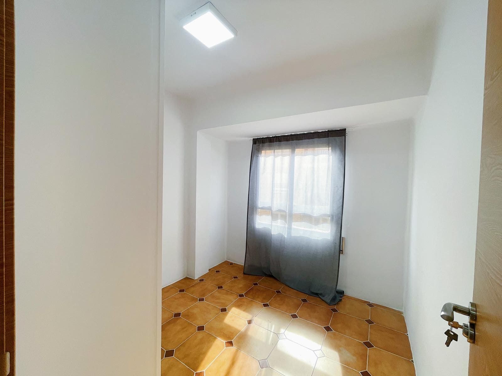 Habitación pequeña y vacía con baldosas estampadas en el suelo y una ventana con cortinas grises.