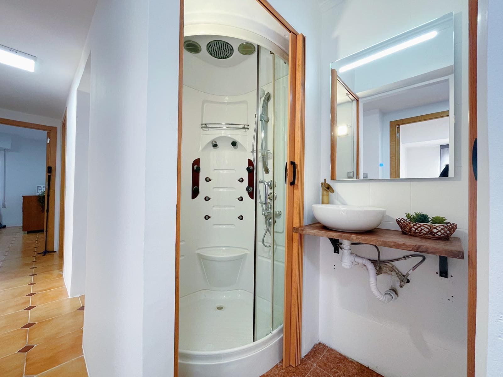 Pequeño baño con ducha, lavabo y espejo.