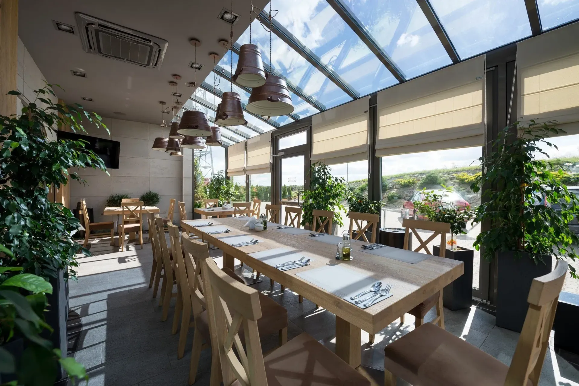 Speisesaal des Restaurants mit einem langen Holztisch für Gäste, Oberlicht und Pflanzen.