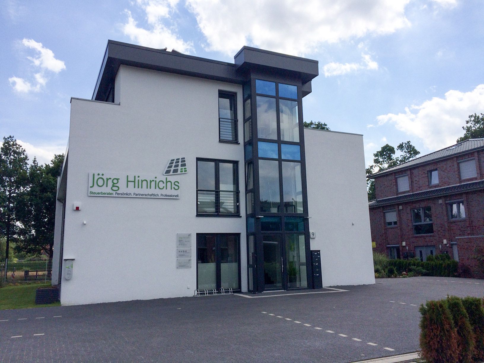 Weißes Gebäude mit Glaseingang und Schild „Jörg Hinrichs“.