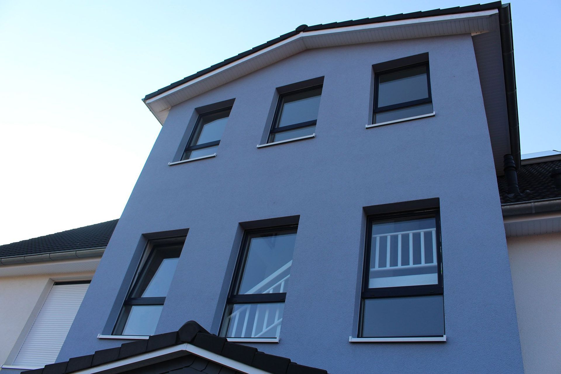 Blaues mehrstöckiges Gebäude mit schwarz gerahmten Fenstern und weißen Verzierungen vor blauem Himmel.