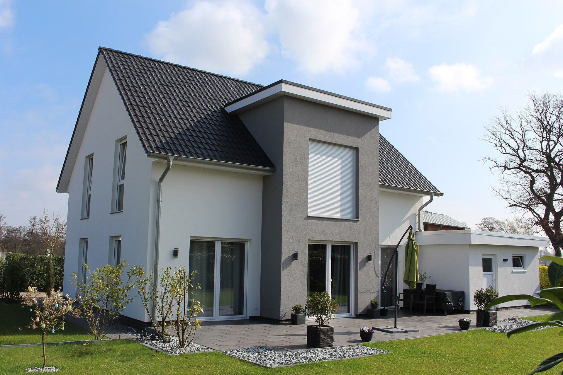 Modernes zweistöckiges Haus mit weiß-grauer Fassade, grauem Dach und gepflegtem Rasen unter blauem Himmel.