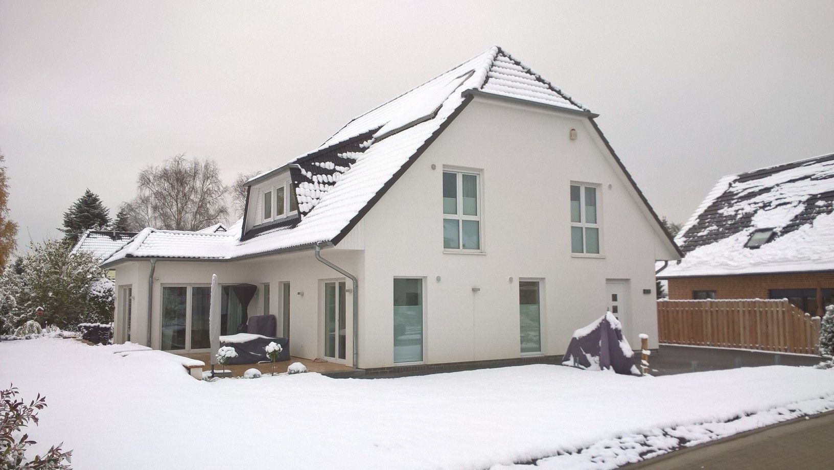 Weißes, schneebedecktes Haus; Auffahrt; bedeckter Himmel.