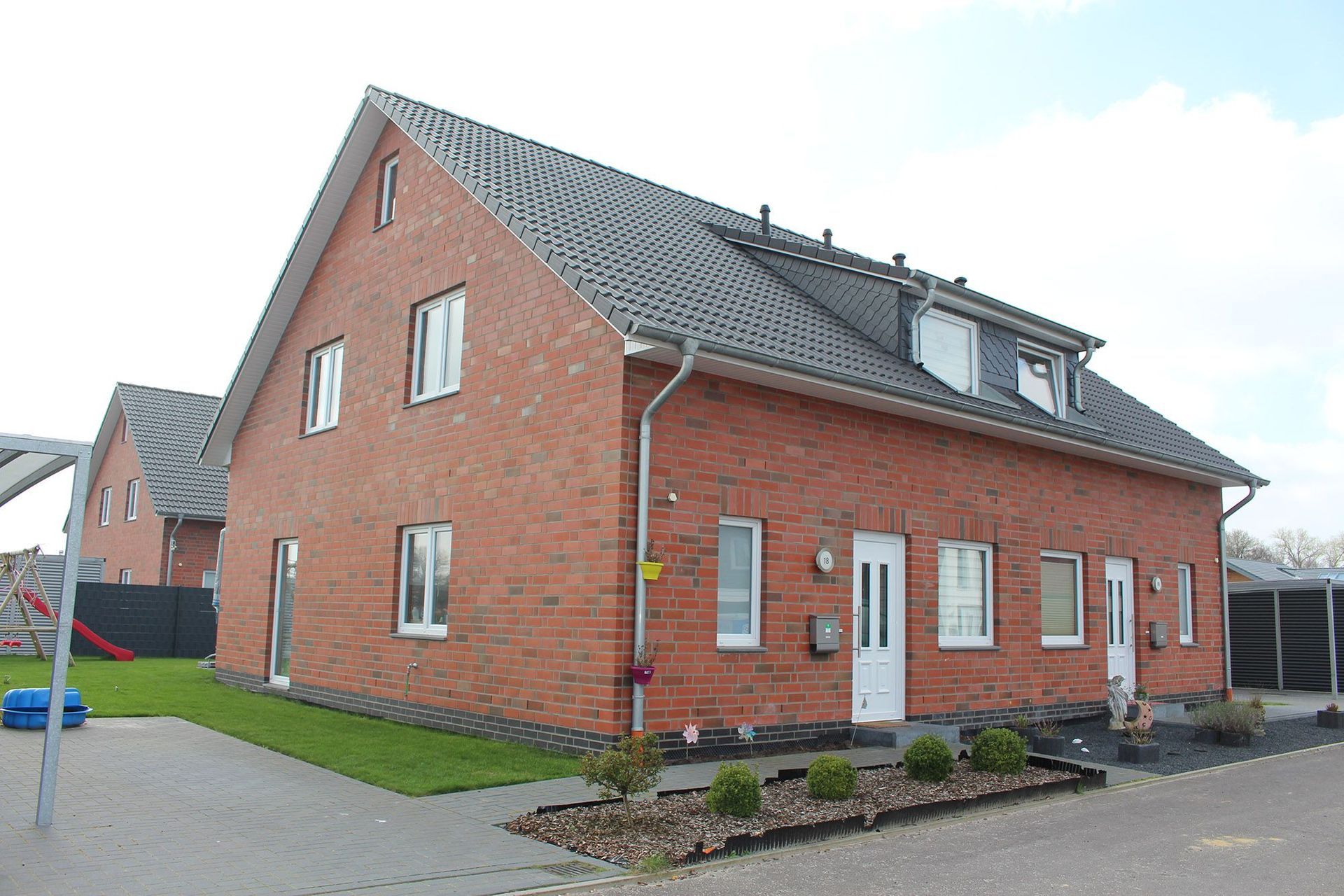 Rotes Backsteinhaus mit weißen Fenstern und Türen; graues Dach; grüner Rasen.