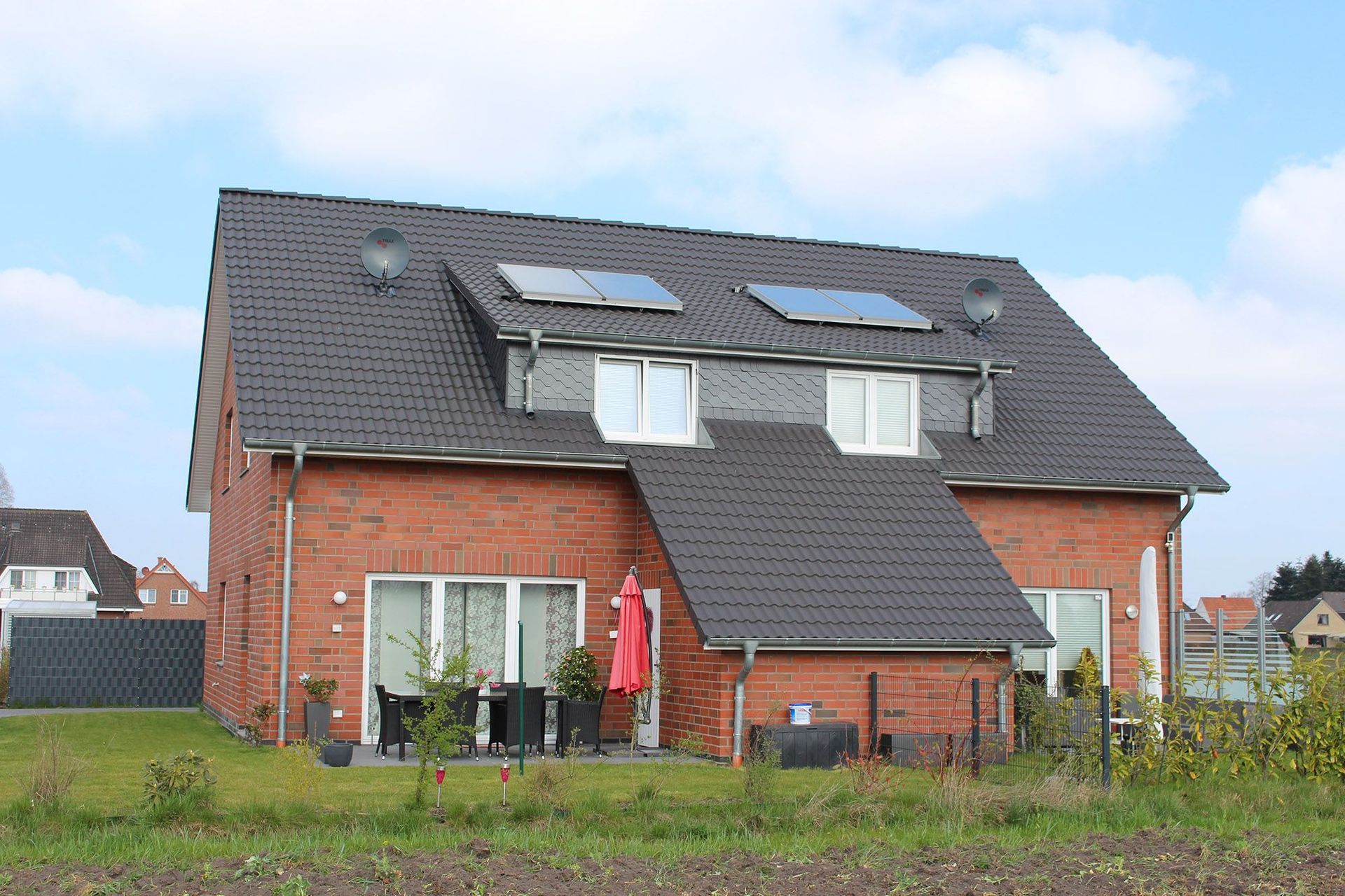 Rotes Backsteinhaus mit grauem Dach und Dachgauben; Terrasse mit Tisch und Stühlen.