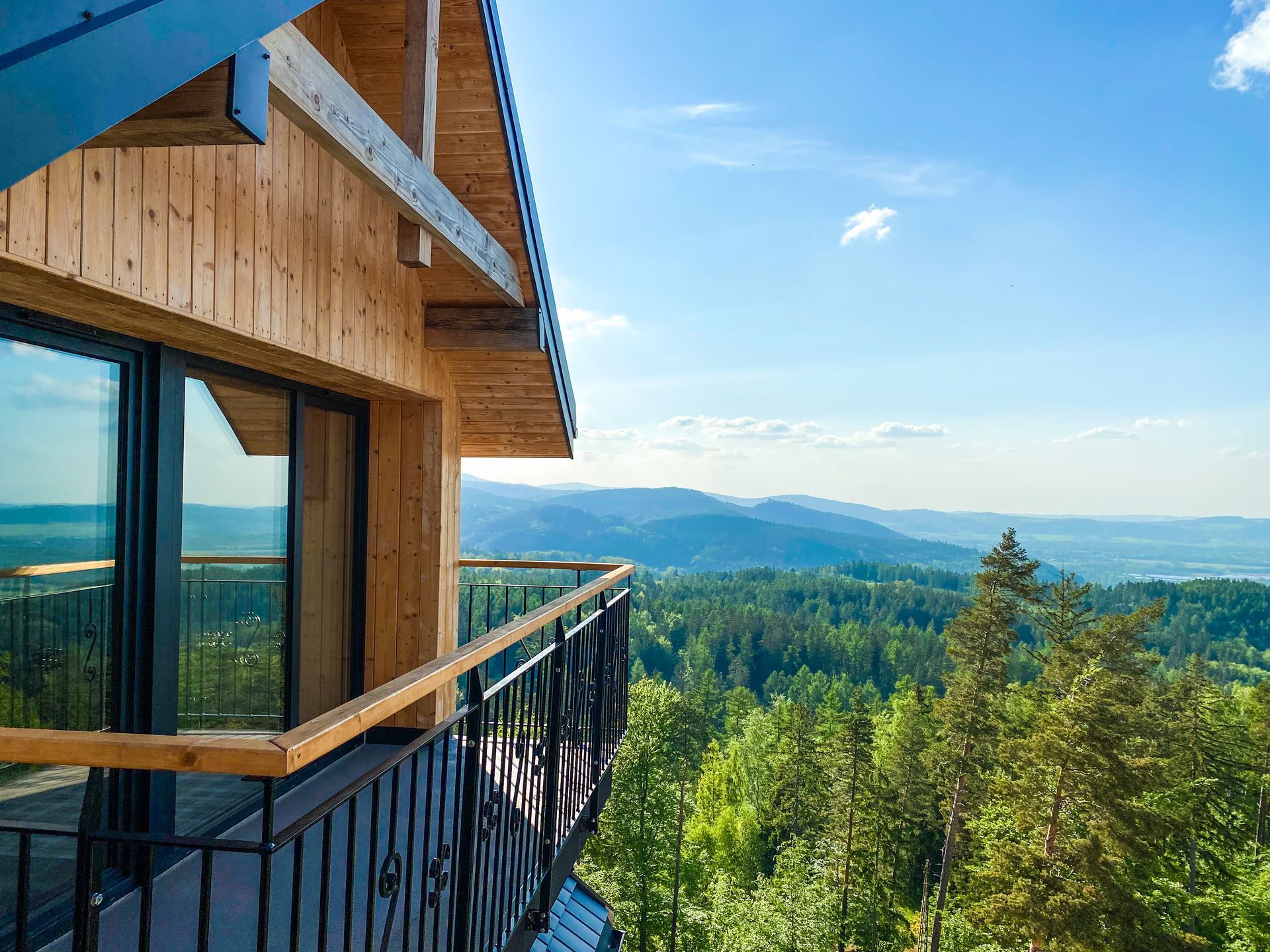 Drewniany balkon w domku z widokiem na zalesiony krajobraz górski pod błękitnym niebem