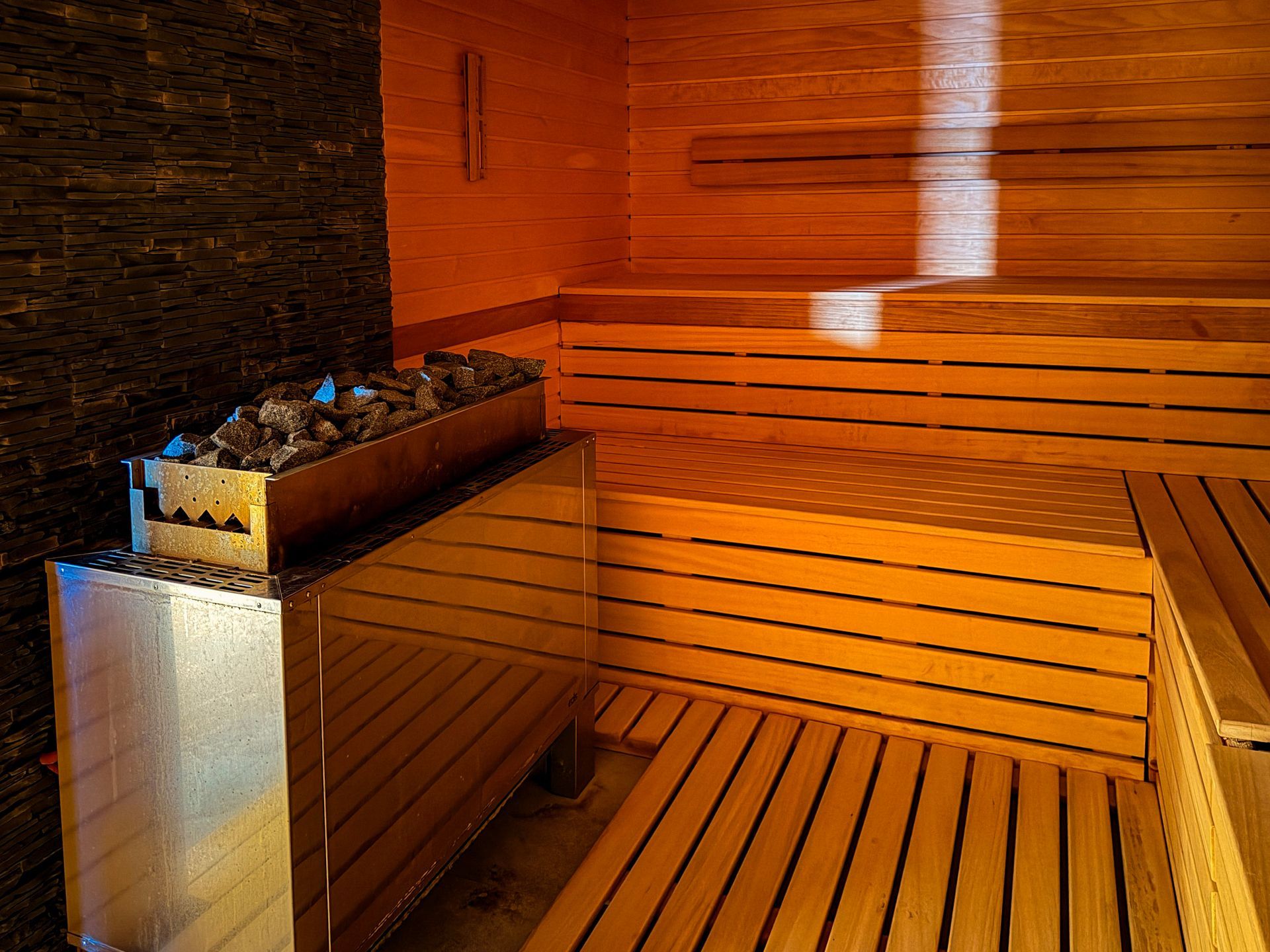 Nowoczesna drewniana sauna z ławkami i metalowym piecem, oświetlona ciepłym światłem słonecznym