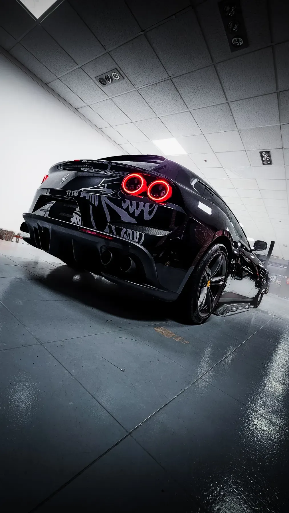 Coche deportivo negro, vista trasera, en ángulo hacia arriba en un garaje, luces iluminadas.