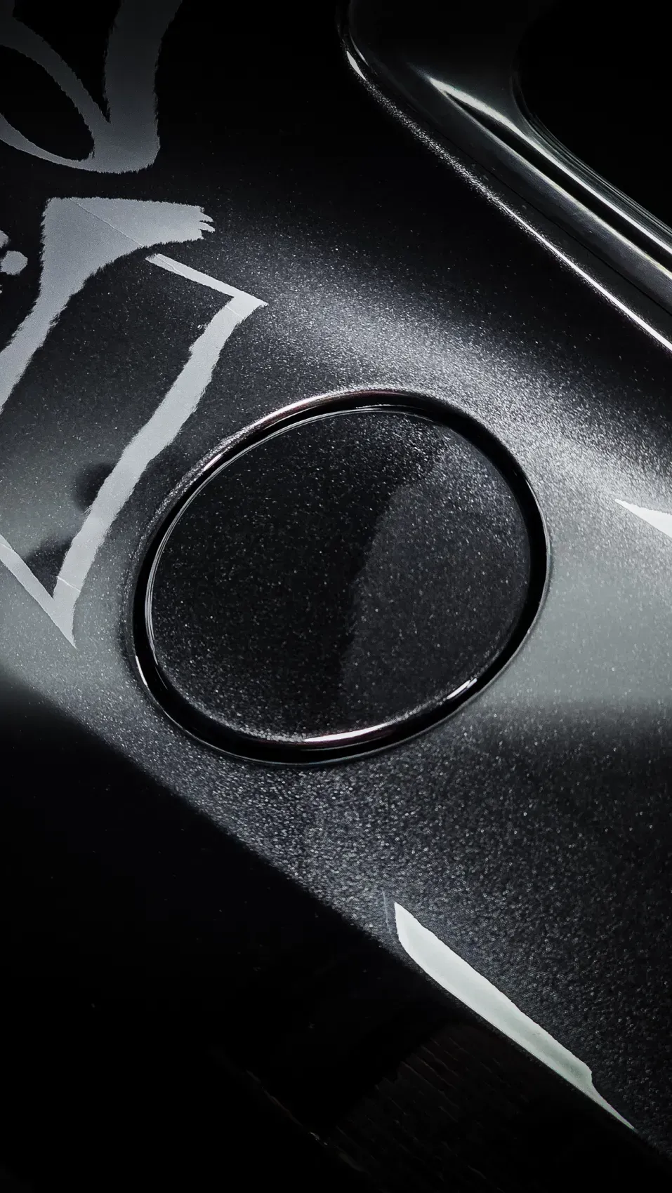 Primer plano de la superficie oscura y brillante de un coche con la tapa del depósito de combustible.