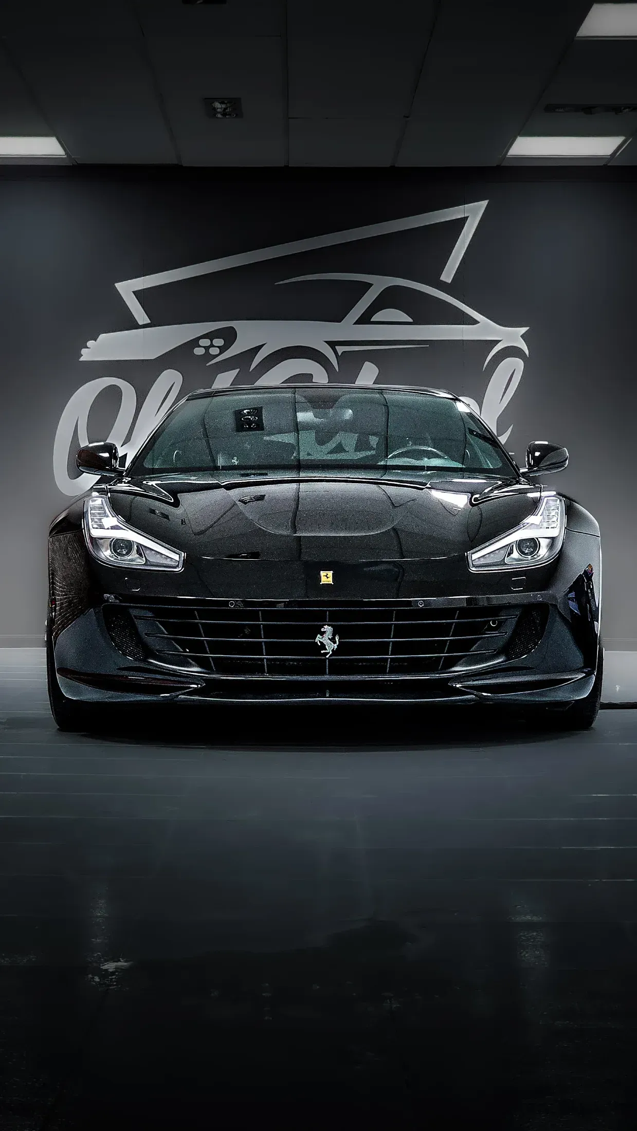 Coche deportivo Ferrari negro aparcado en un garaje con el logotipo del coche en la pared.