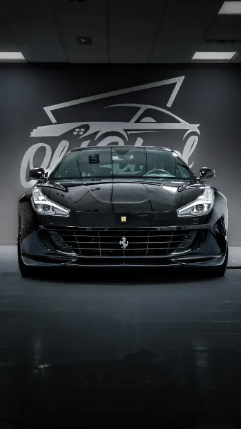 Coche deportivo Ferrari negro aparcado en un garaje con el logotipo del coche en la pared.
