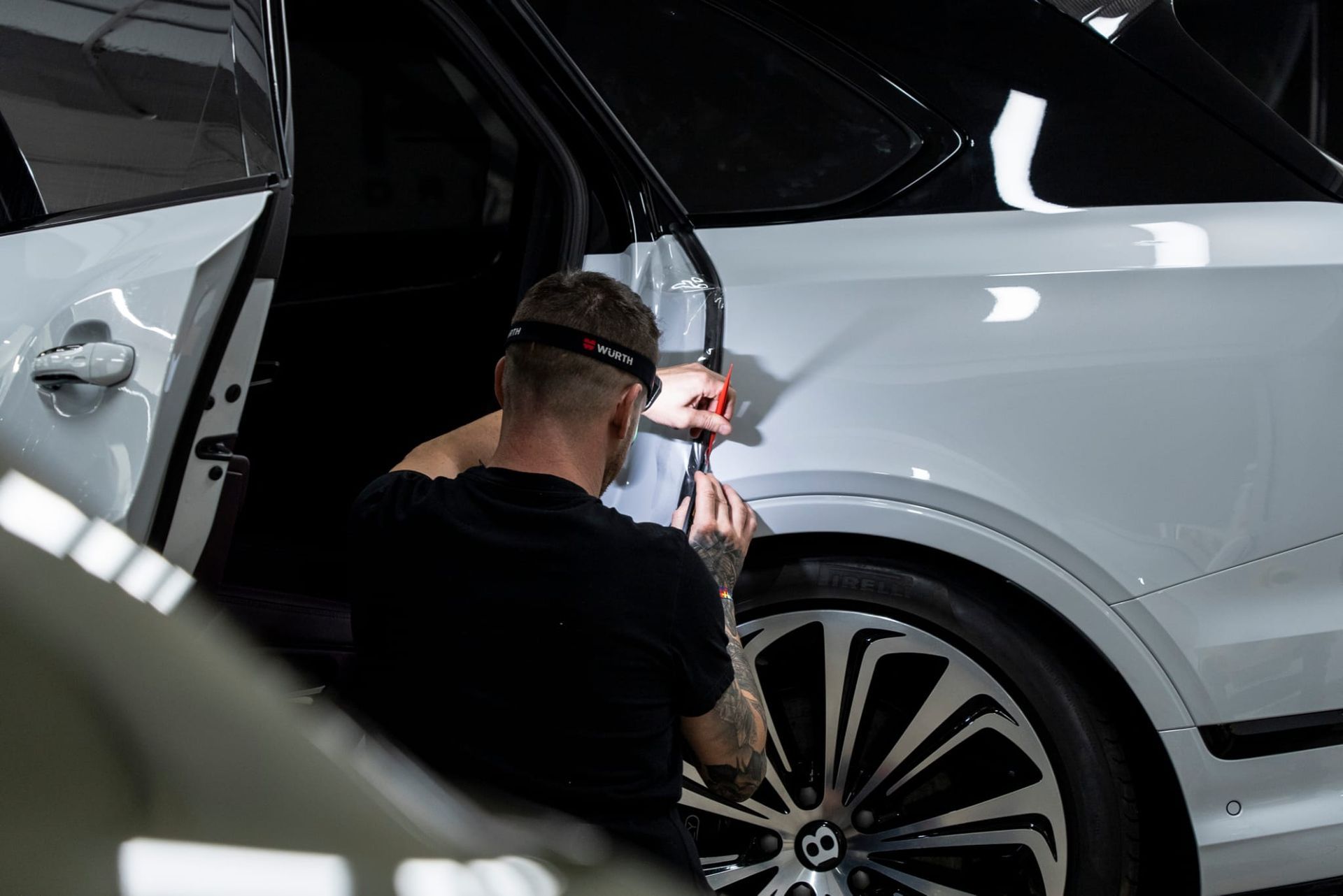 Persona trabajando en un coche blanco, posiblemente aplicando película, en un taller.